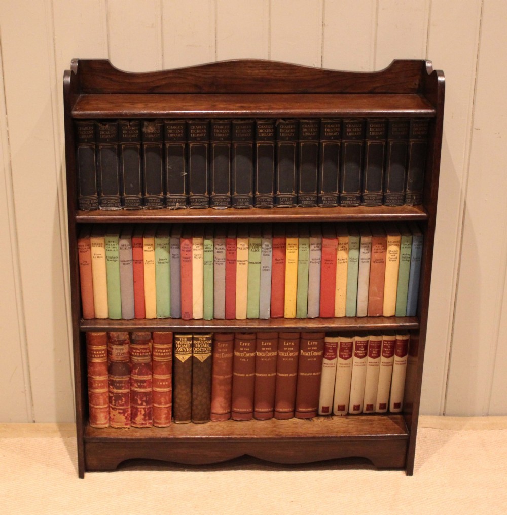 A dark oak open bookcase with three shelves filled with books, featuring a gently curved top cresting and shaped apron. View III