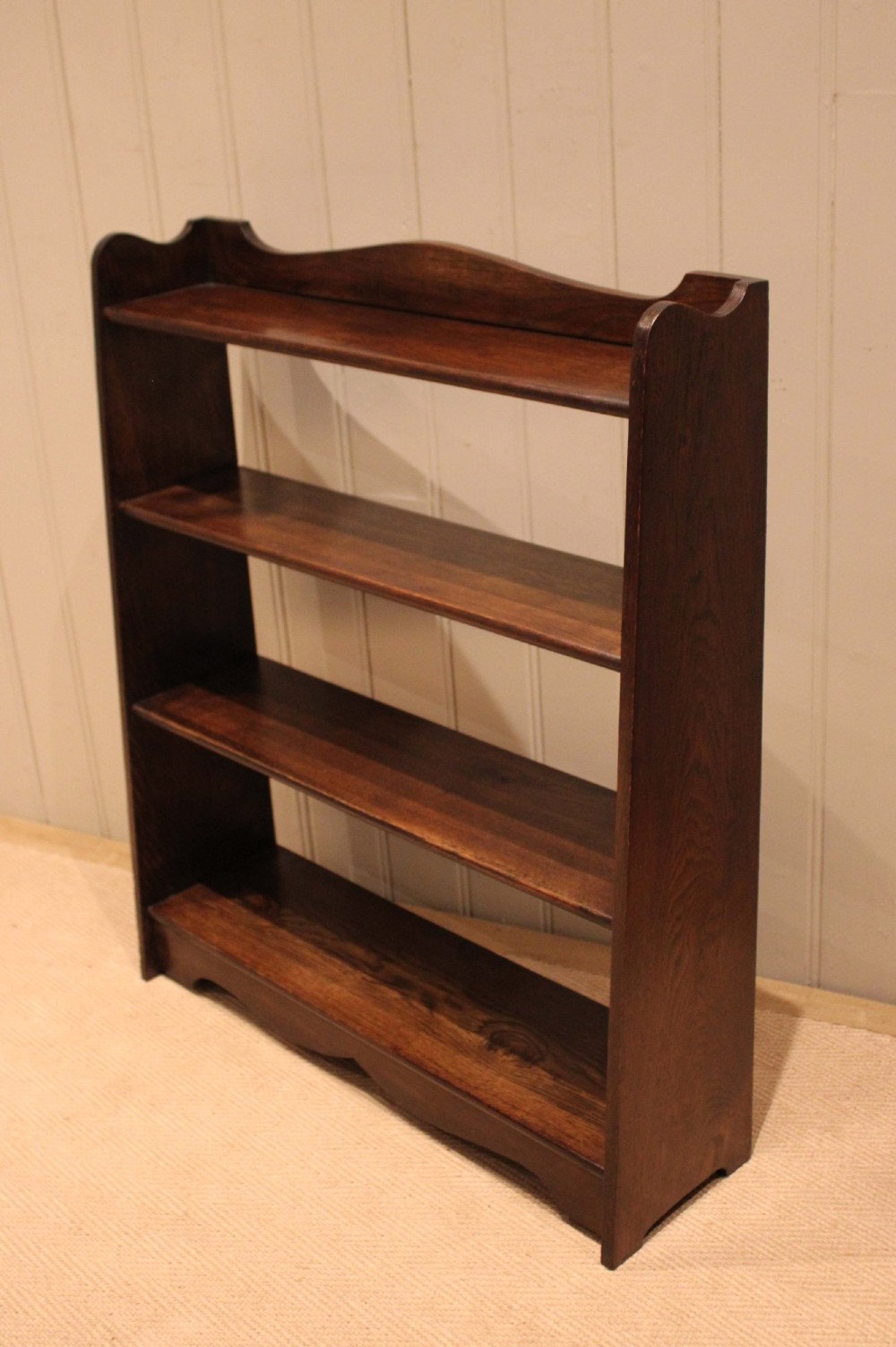 A dark oak open bookcase with three shelves filled with books, featuring a gently curved top cresting and shaped apron. View IV