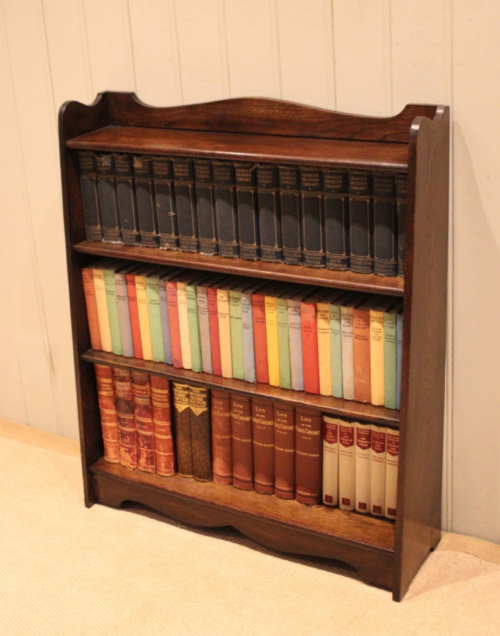 A dark oak open bookcase with three shelves filled with books, featuring a gently curved top cresting and shaped apron. View V
