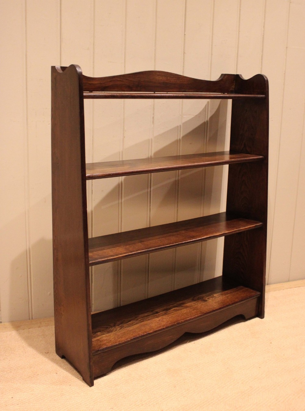 A dark oak open bookcase with three shelves filled with books, featuring a gently curved top cresting and shaped apron. View VI