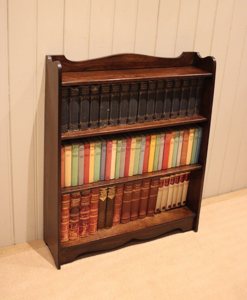 A dark oak open bookcase with three shelves filled with books, featuring a gently curved top cresting and shaped apron. View VII