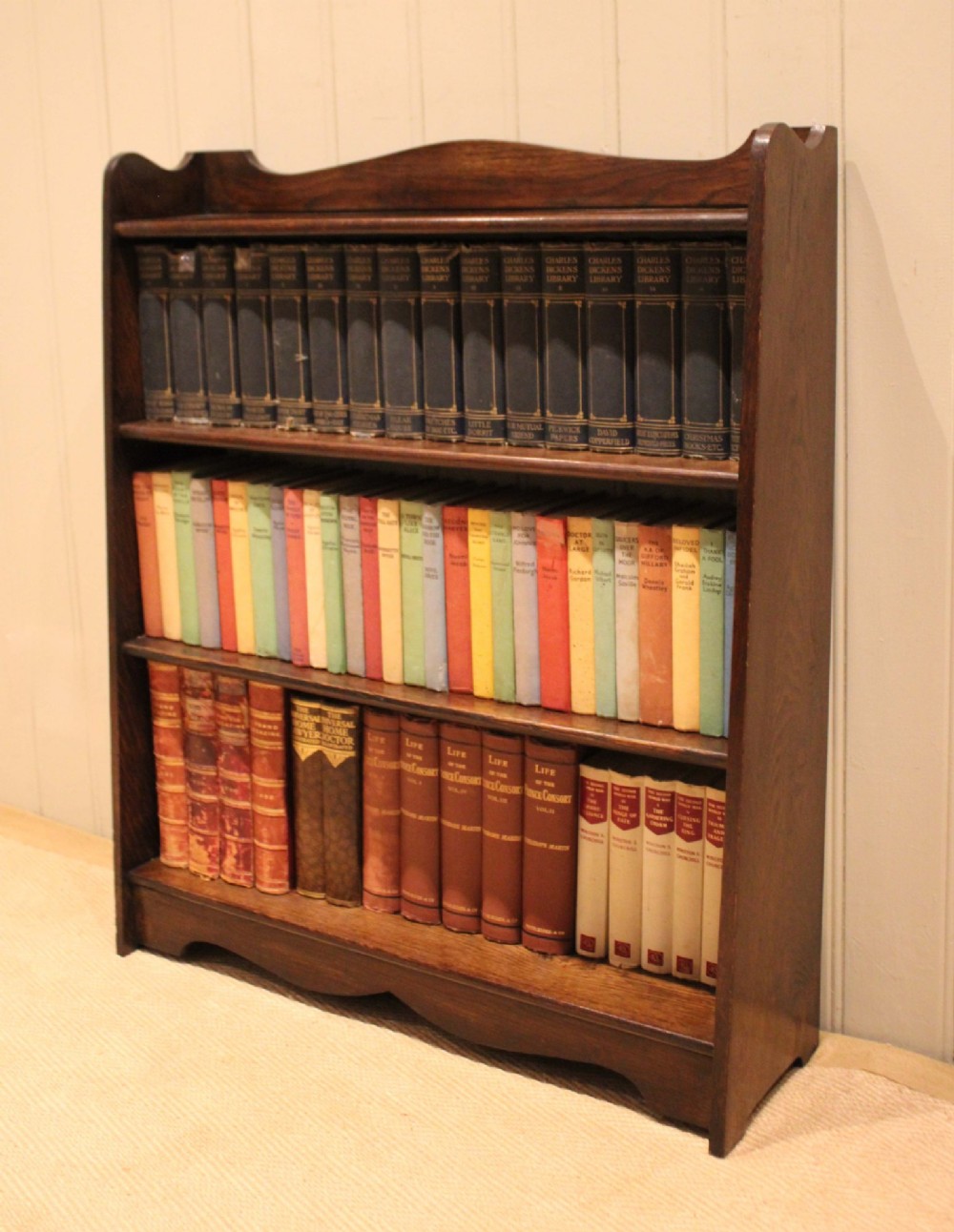 A dark oak open bookcase with three shelves filled with books, featuring a gently curved top cresting and shaped apron. View IX