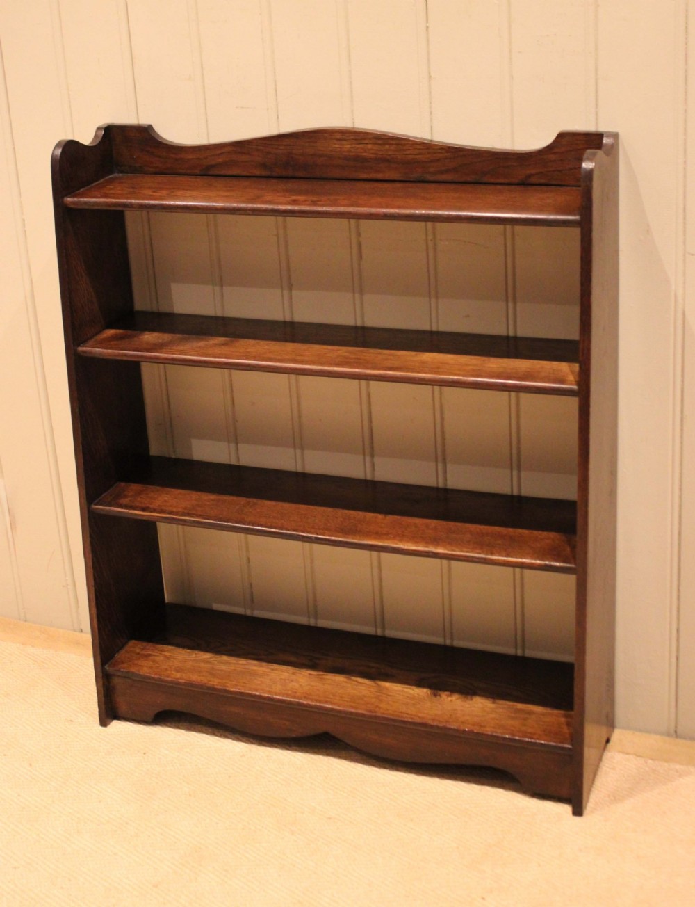 A dark oak open bookcase with three shelves filled with books, featuring a gently curved top cresting and shaped apron. View X