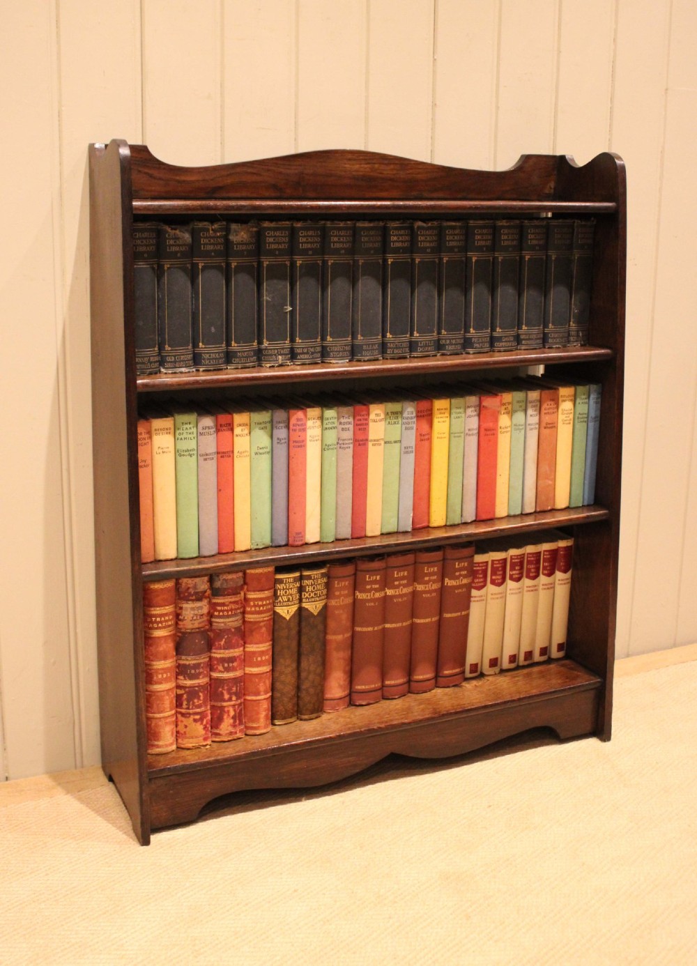 A dark oak open bookcase with three shelves filled with books, featuring a gently curved top cresting and shaped apron. View XI