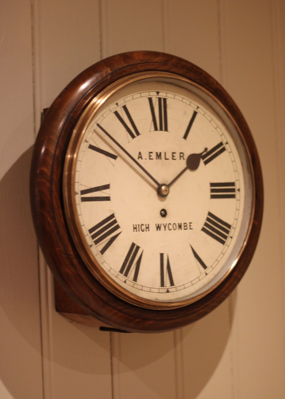An antique circular wall clock featuring a turned dark beech frame, brass bezel, and painted white dial with Roman numerals. View IV