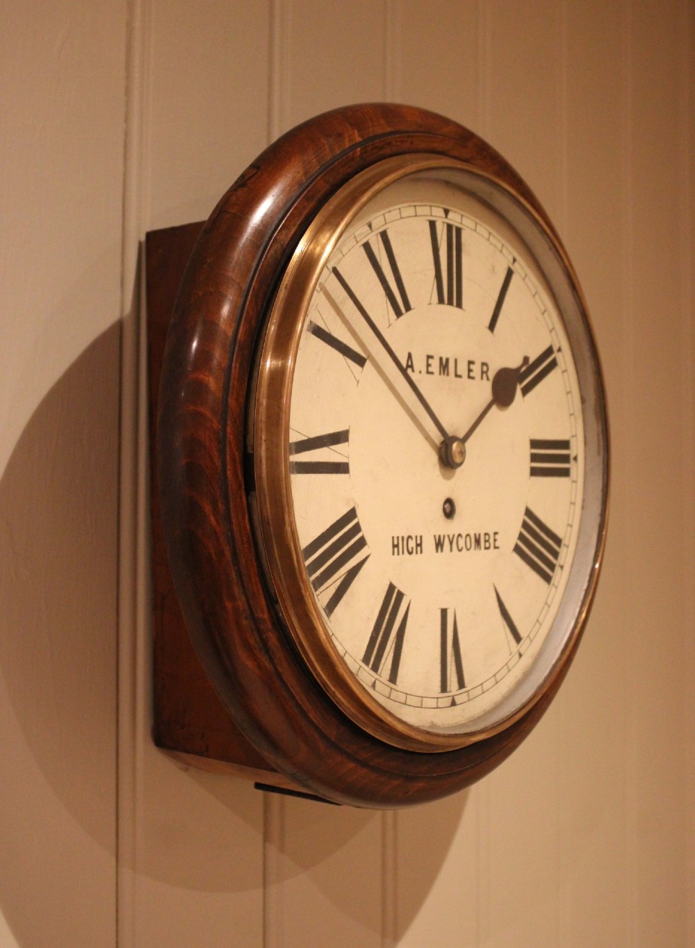 An antique circular wall clock featuring a turned dark beech frame, brass bezel, and painted white dial with Roman numerals. View V