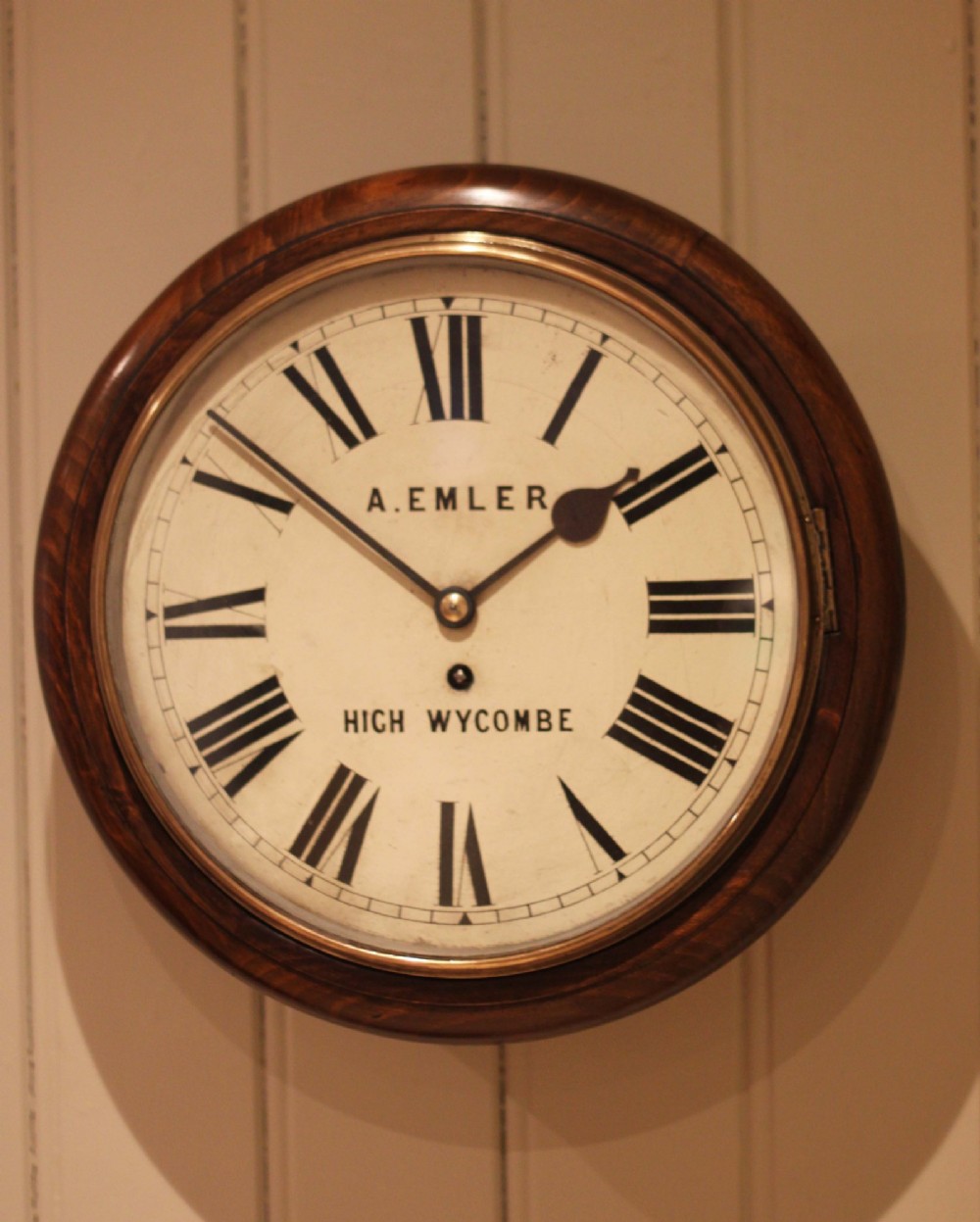 An antique circular wall clock featuring a turned dark beech frame, brass bezel, and painted white dial with Roman numerals. View VII