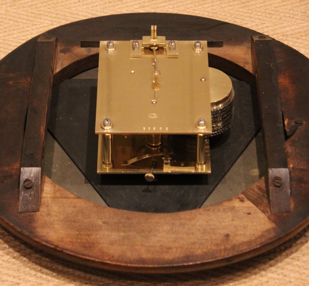 An antique circular wall clock featuring a turned dark beech frame, brass bezel, and painted white dial with Roman numerals. View XII