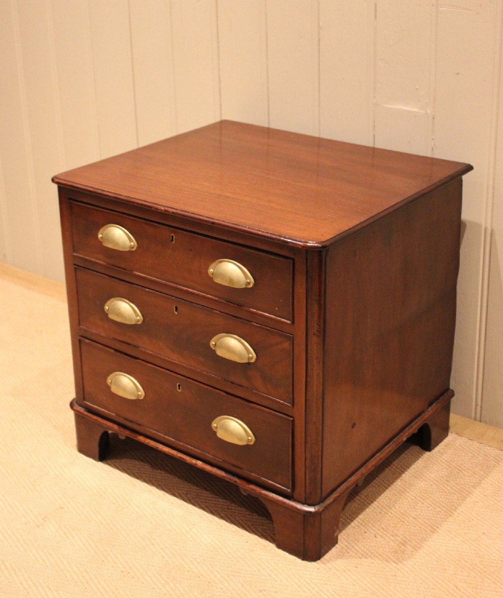 A mid-19th century small low mahogany chest of drawers featuring three graduated drawers with brass cup handles and bracket feet.
