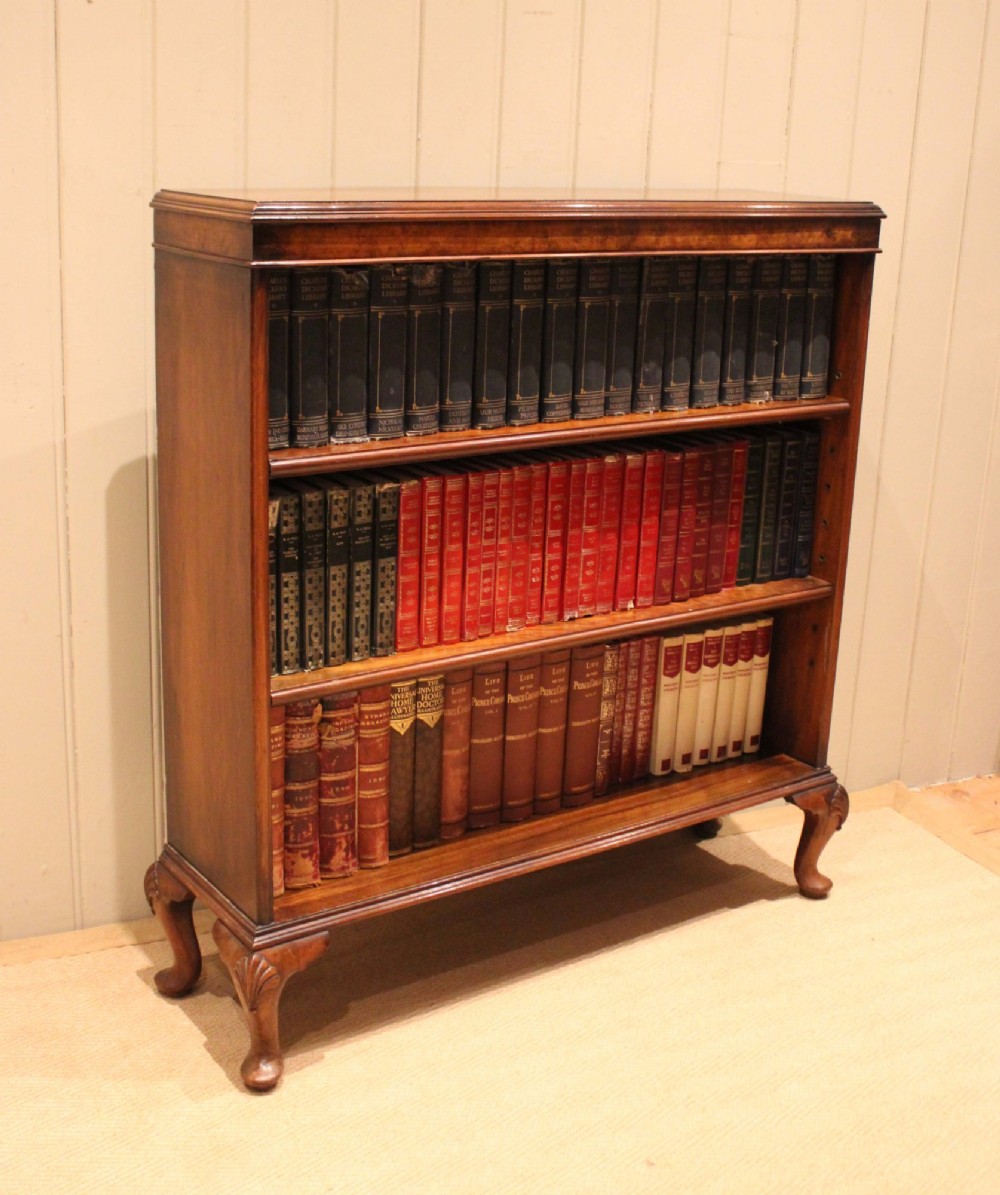 A low antique open walnut bookcase featuring three tiers of books and resting on carved cabriole legs.