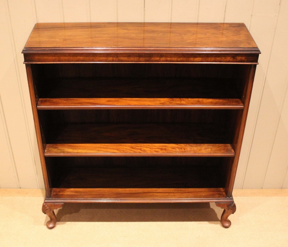 A low antique open walnut bookcase featuring three tiers of books and resting on carved cabriole legs. View VI