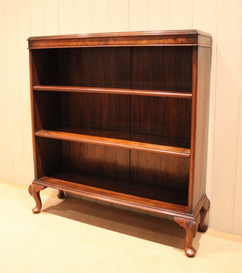 A low antique open walnut bookcase featuring three tiers of books and resting on carved cabriole legs. View X