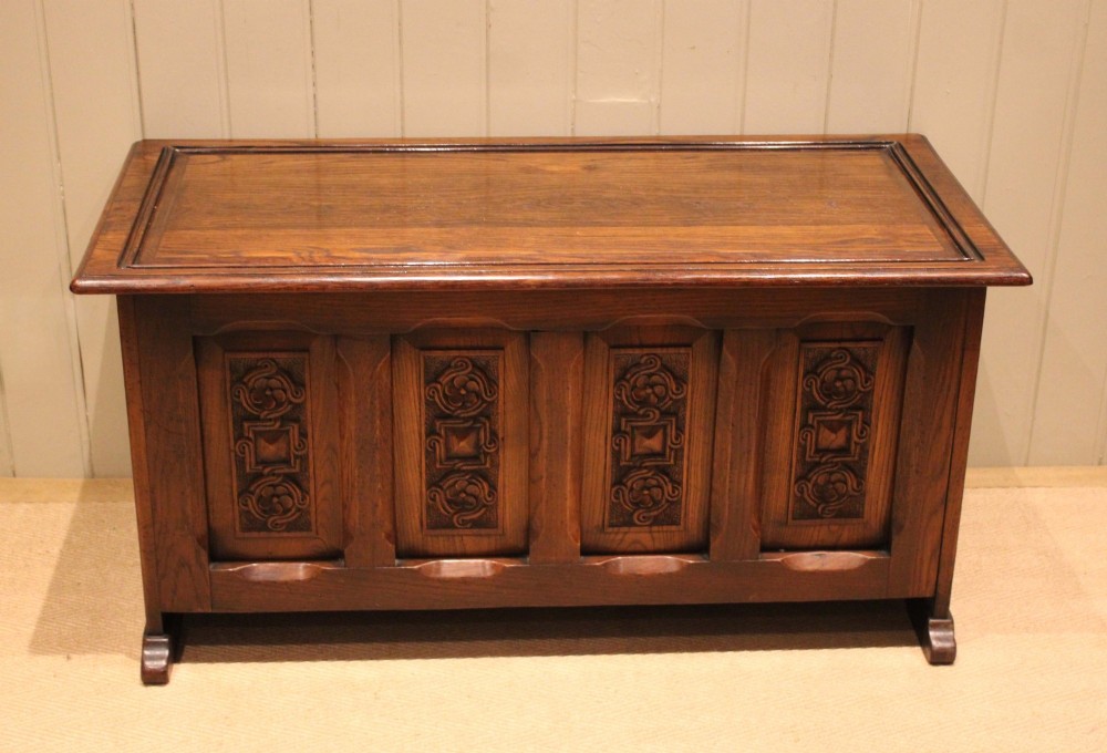 A dark solid oak storage coffer featuring a hinged rectangular lid and four relief-carved front panels.
