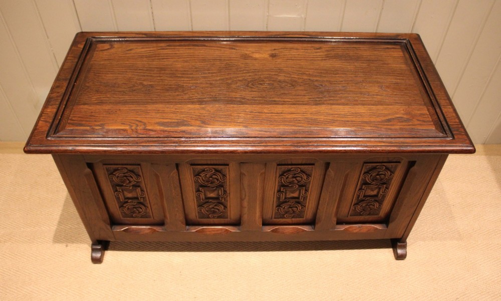 A dark solid oak storage coffer featuring a hinged rectangular lid and four relief-carved front panels. View II