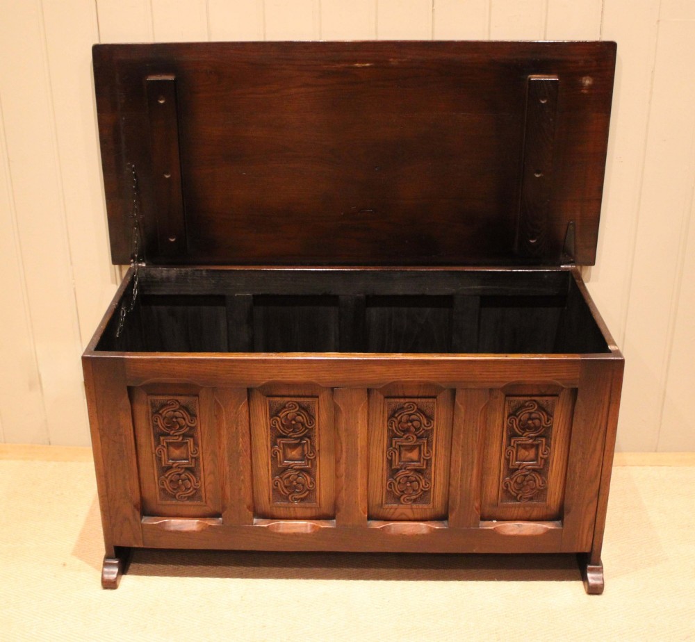 A dark solid oak storage coffer featuring a hinged rectangular lid and four relief-carved front panels. View III