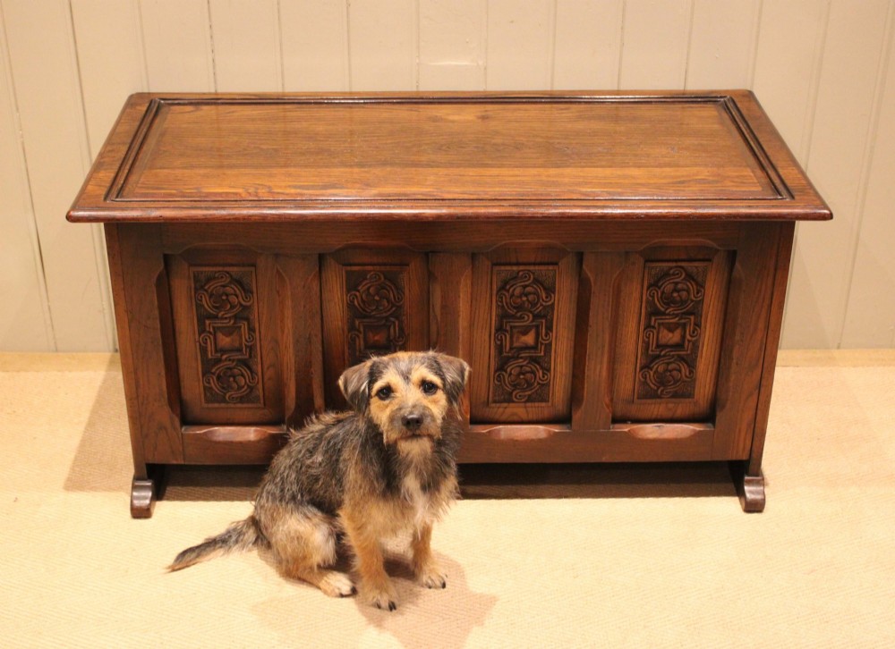 A dark solid oak storage coffer featuring a hinged rectangular lid and four relief-carved front panels. View V