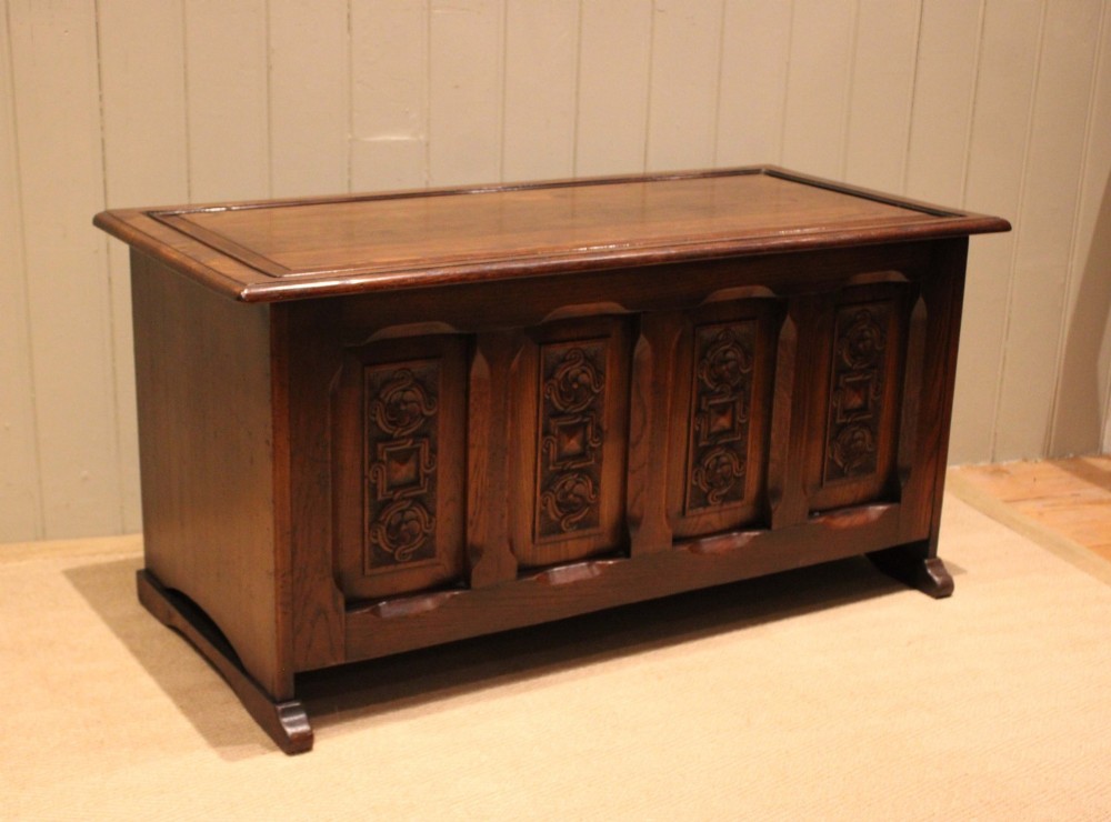A dark solid oak storage coffer featuring a hinged rectangular lid and four relief-carved front panels. View VI