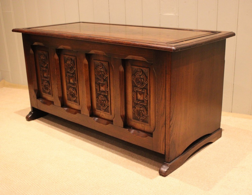 A dark solid oak storage coffer featuring a hinged rectangular lid and four relief-carved front panels. View VII
