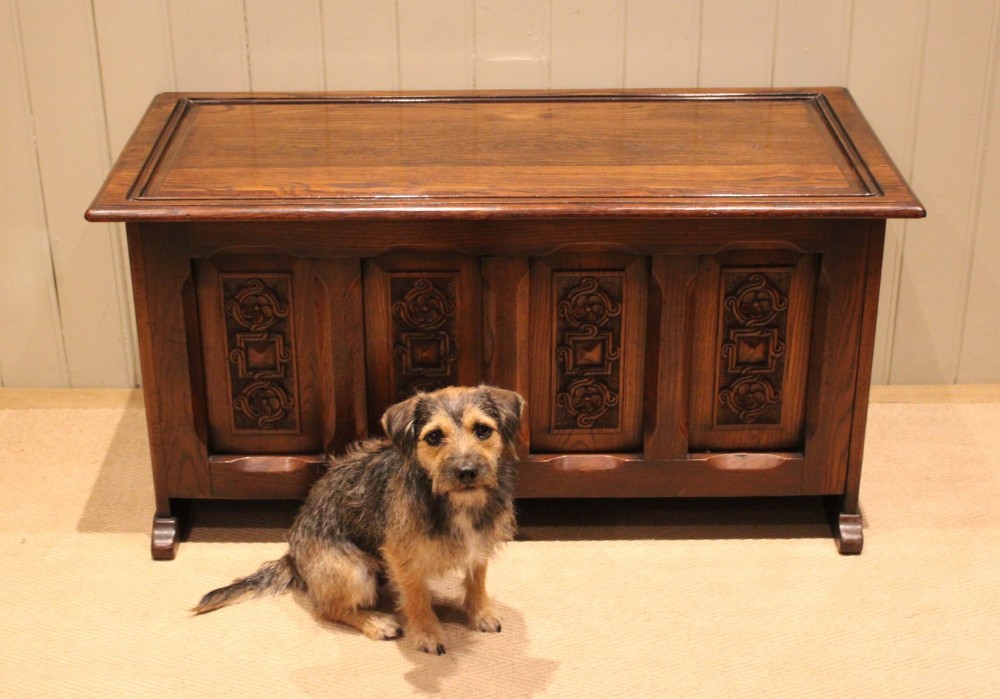 A dark solid oak storage coffer featuring a hinged rectangular lid and four relief-carved front panels. View VIII