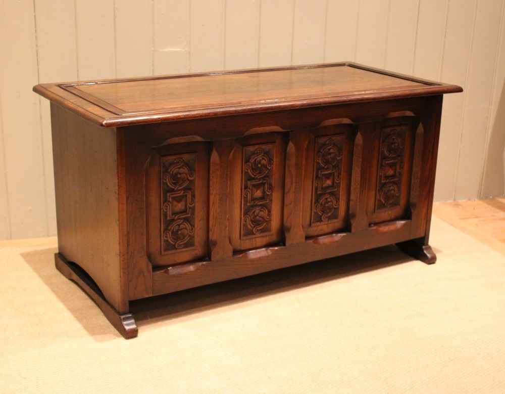 A dark solid oak storage coffer featuring a hinged rectangular lid and four relief-carved front panels. View IX