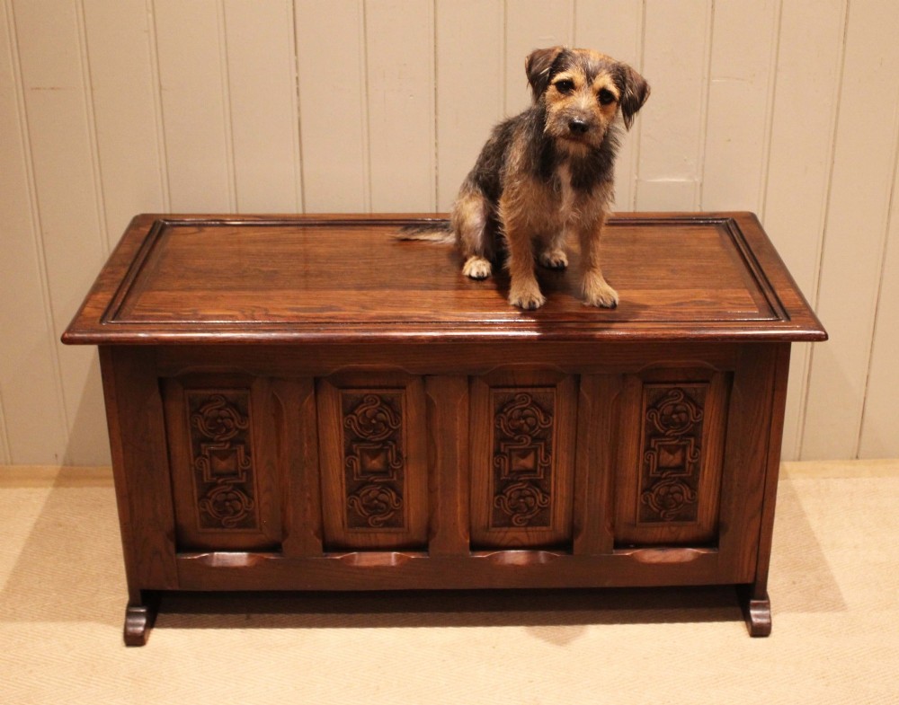 A dark solid oak storage coffer featuring a hinged rectangular lid and four relief-carved front panels. View X