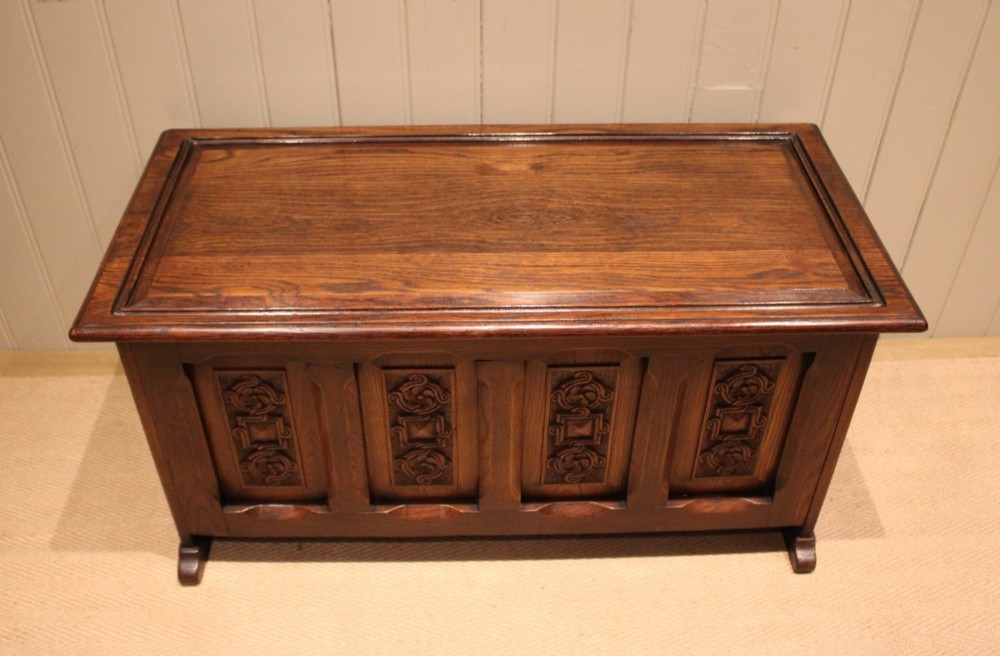A dark solid oak storage coffer featuring a hinged rectangular lid and four relief-carved front panels. View XI