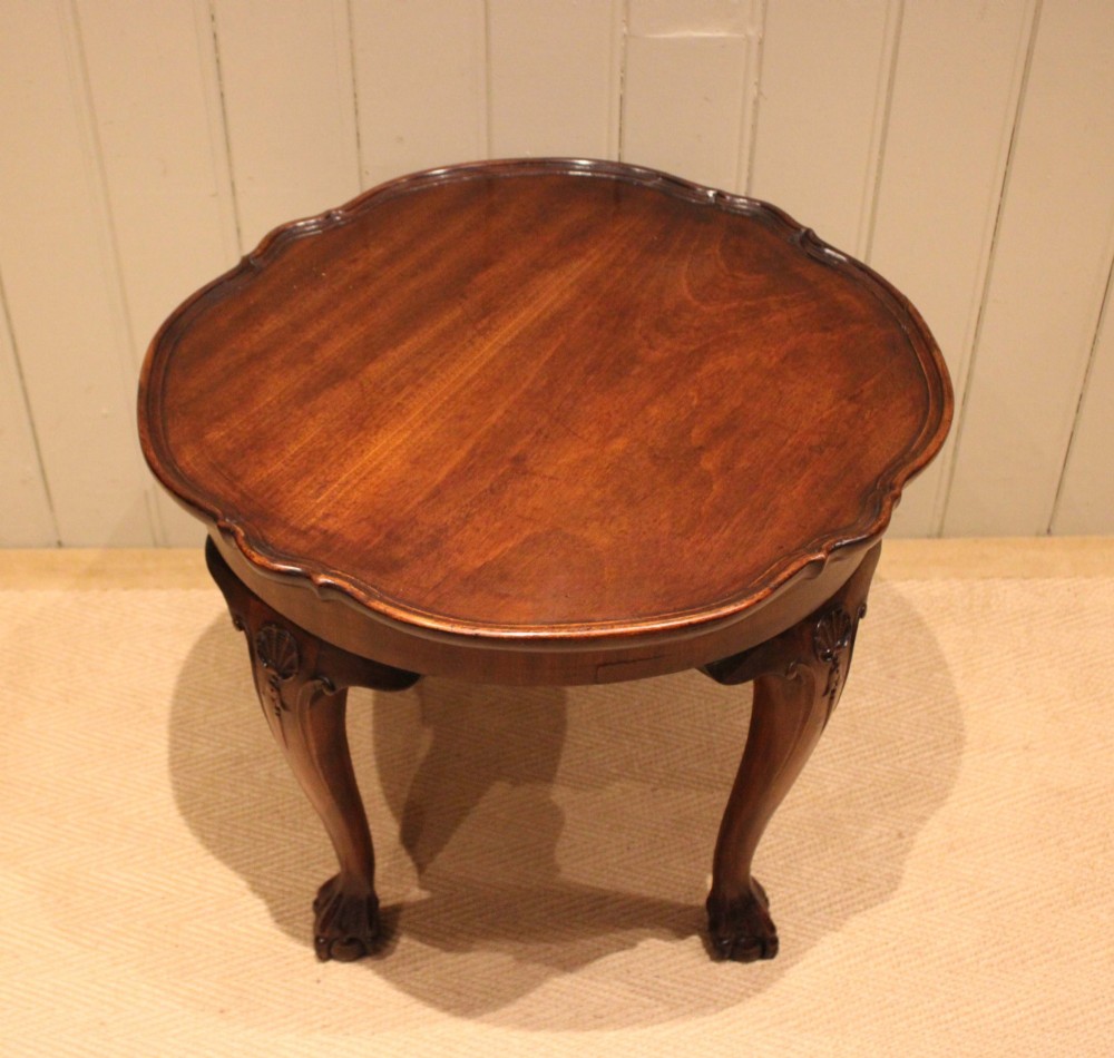 A low mahogany coffee table featuring a shaped piecrust rim, carved cabriole legs with shell knee detailing, and claw and ball feet.
