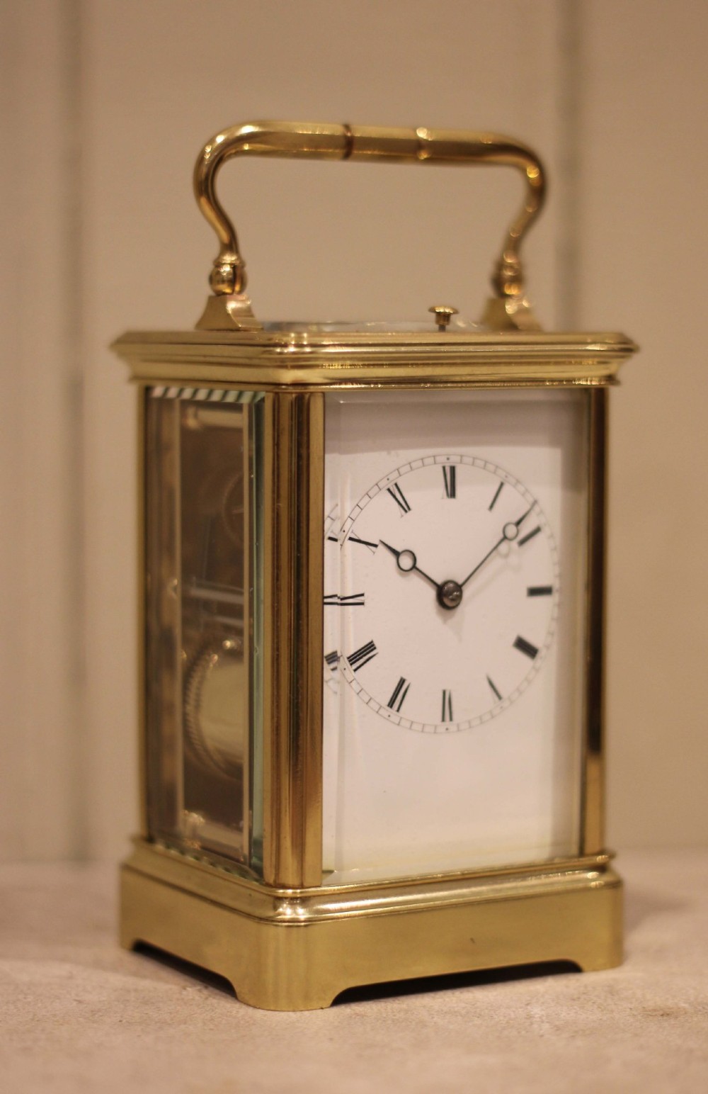 A nineteenth-century French polished brass carriage clock featuring bevelled glass side panels, a white enamel dial with Roman numerals, and a hinged top carrying handle.