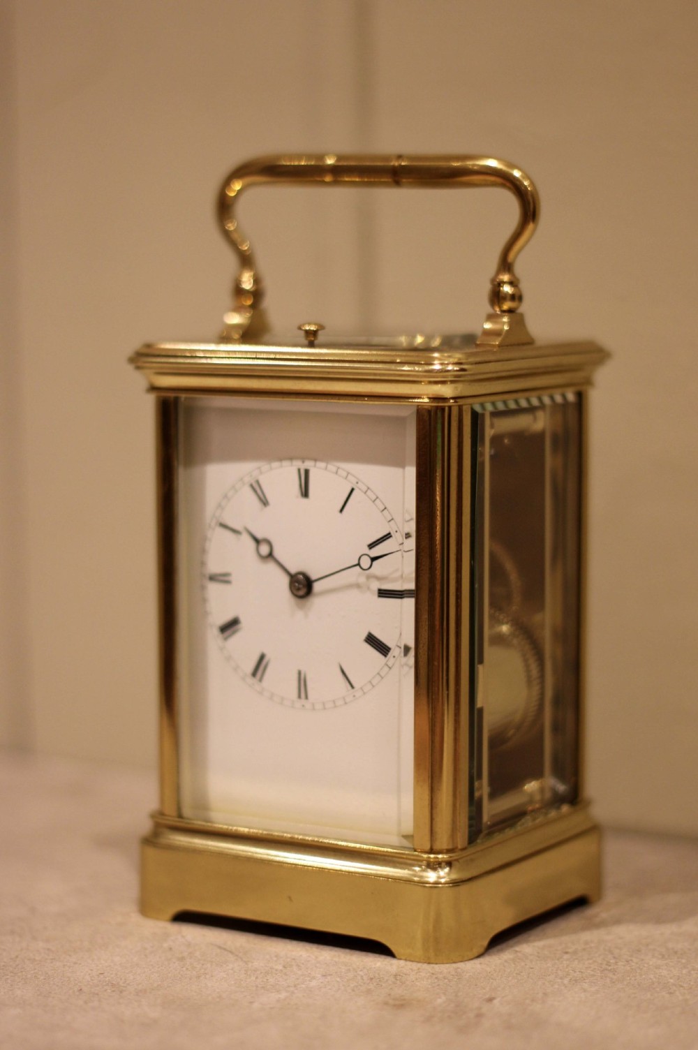 A nineteenth-century French polished brass carriage clock featuring bevelled glass side panels, a white enamel dial with Roman numerals, and a hinged top carrying handle. View III
