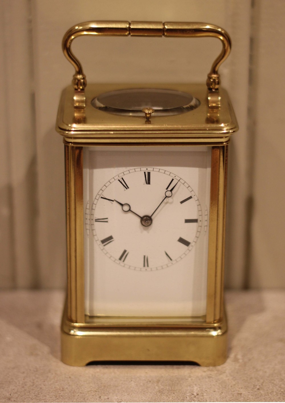 A nineteenth-century French polished brass carriage clock featuring bevelled glass side panels, a white enamel dial with Roman numerals, and a hinged top carrying handle. View IV