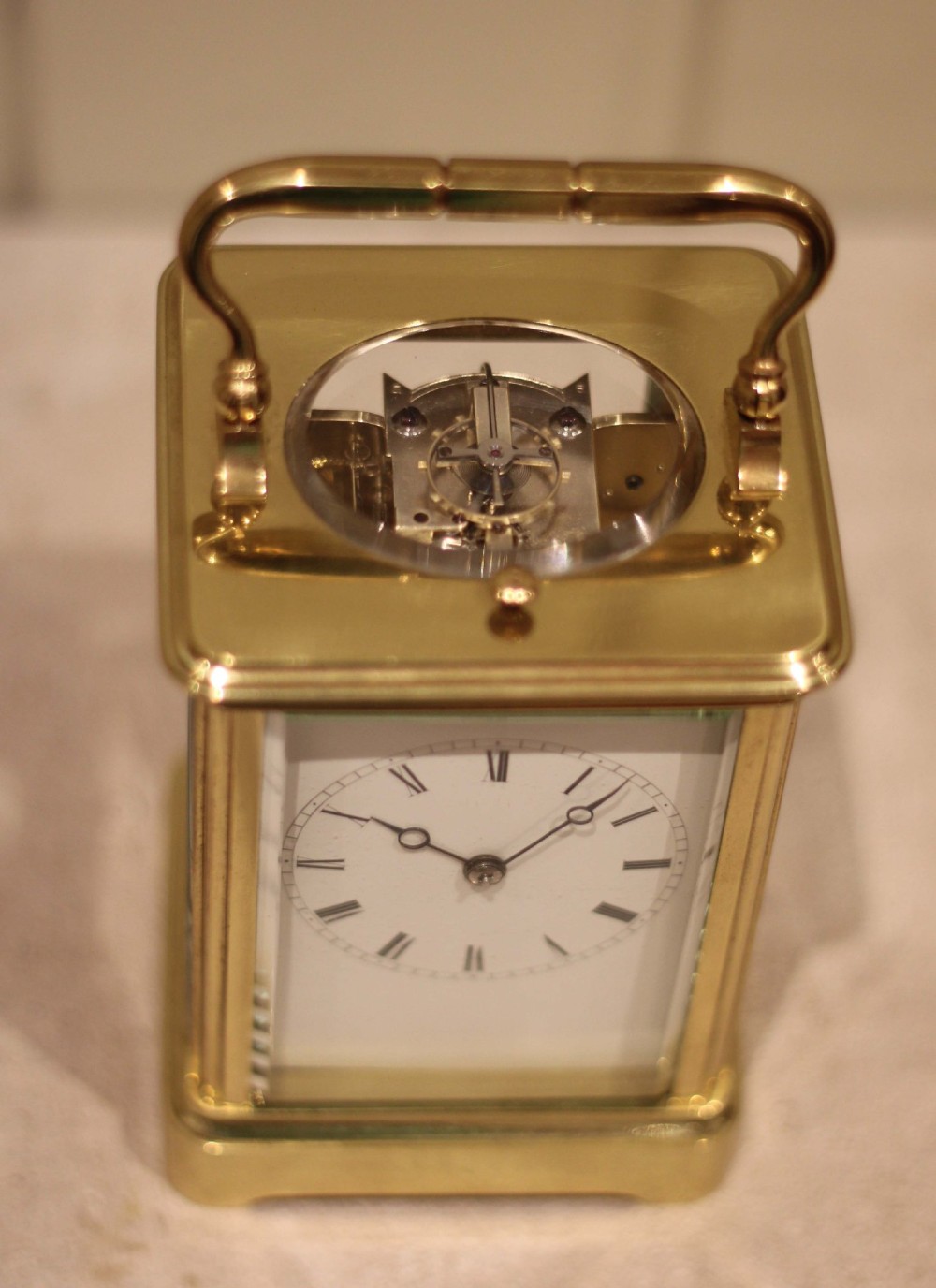 A nineteenth-century French polished brass carriage clock featuring bevelled glass side panels, a white enamel dial with Roman numerals, and a hinged top carrying handle. View V