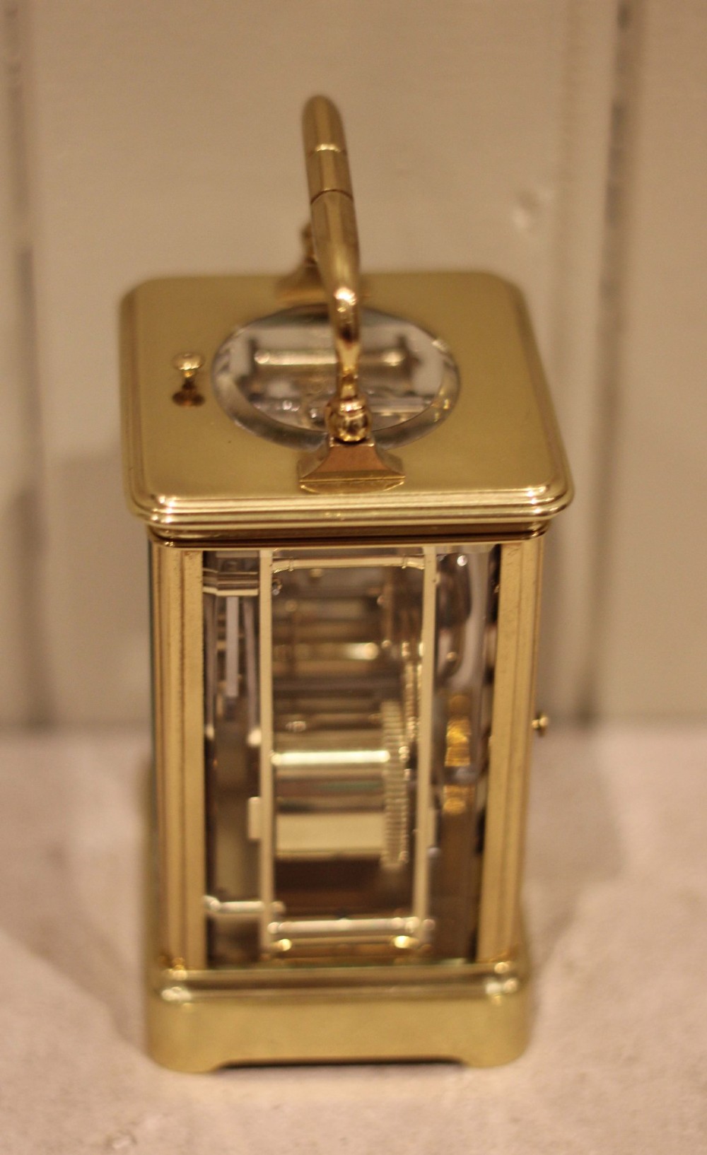 A nineteenth-century French polished brass carriage clock featuring bevelled glass side panels, a white enamel dial with Roman numerals, and a hinged top carrying handle. View VI