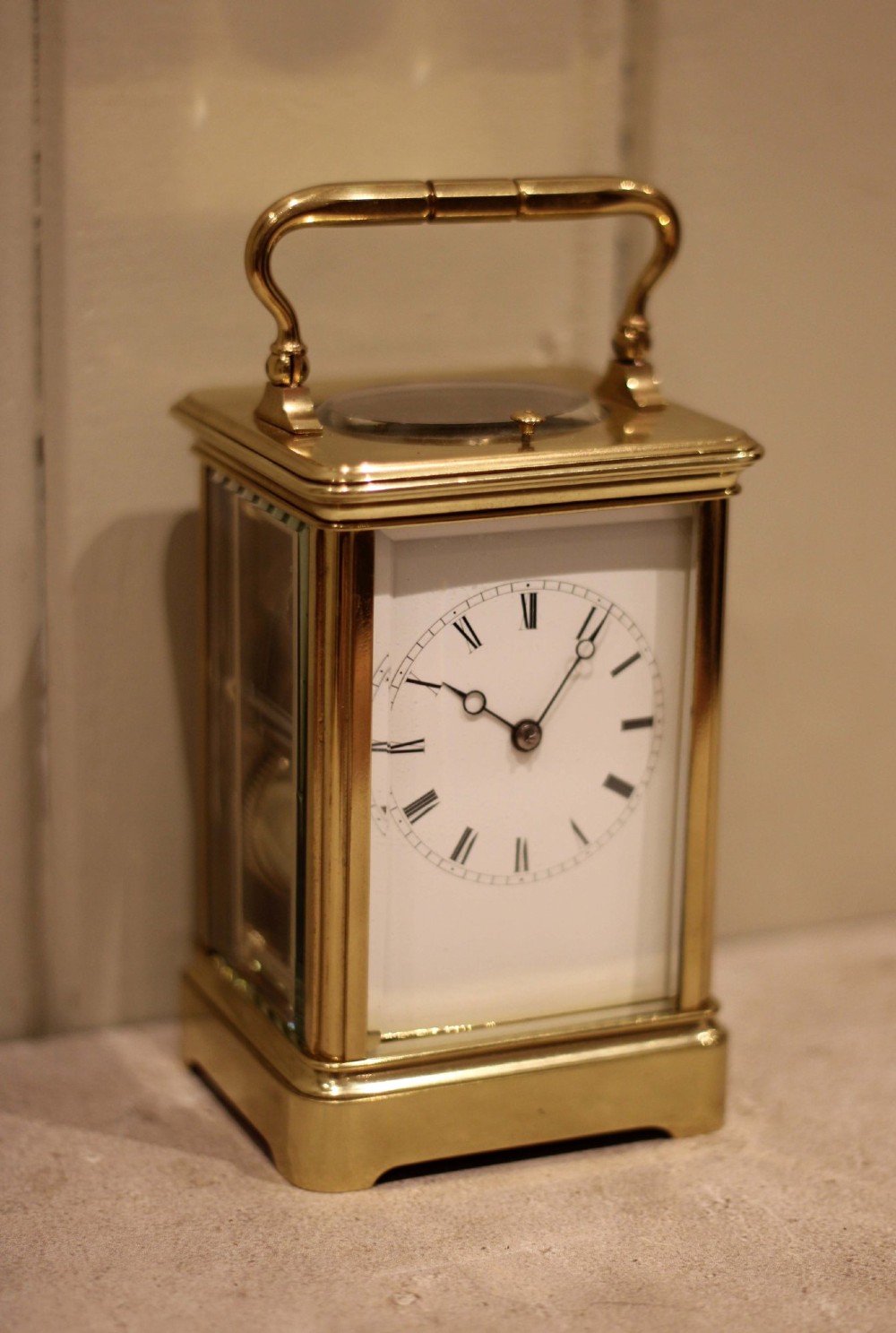 A nineteenth-century French polished brass carriage clock featuring bevelled glass side panels, a white enamel dial with Roman numerals, and a hinged top carrying handle. View VII