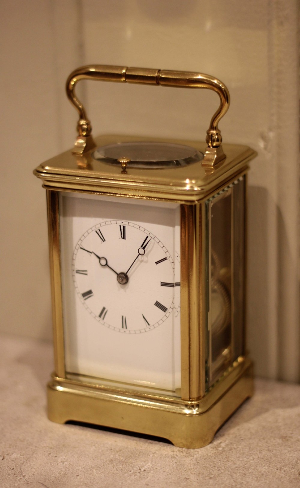 A nineteenth-century French polished brass carriage clock featuring bevelled glass side panels, a white enamel dial with Roman numerals, and a hinged top carrying handle. View VIII