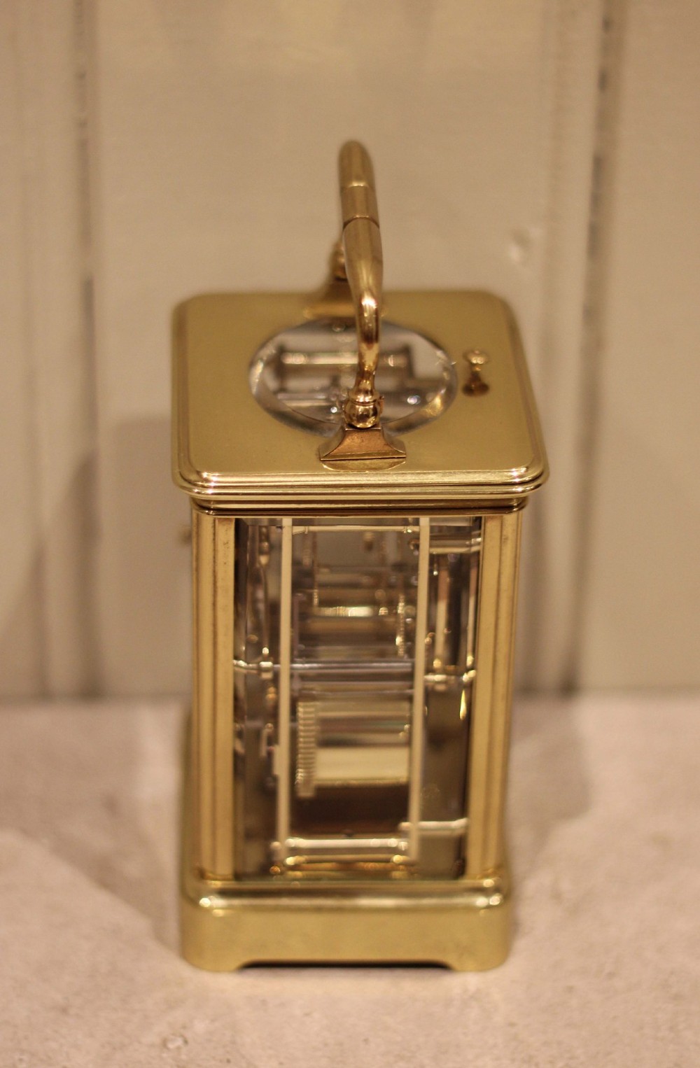A nineteenth-century French polished brass carriage clock featuring bevelled glass side panels, a white enamel dial with Roman numerals, and a hinged top carrying handle. View IX