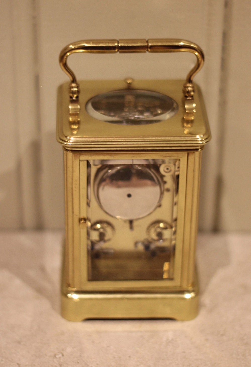 A nineteenth-century French polished brass carriage clock featuring bevelled glass side panels, a white enamel dial with Roman numerals, and a hinged top carrying handle. View X