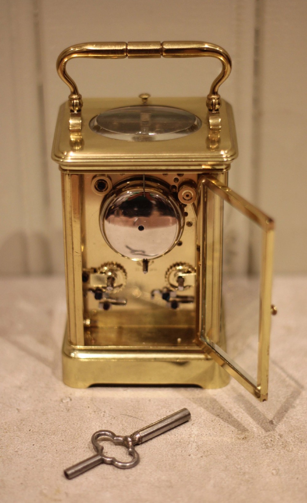 A nineteenth-century French polished brass carriage clock featuring bevelled glass side panels, a white enamel dial with Roman numerals, and a hinged top carrying handle. View XI