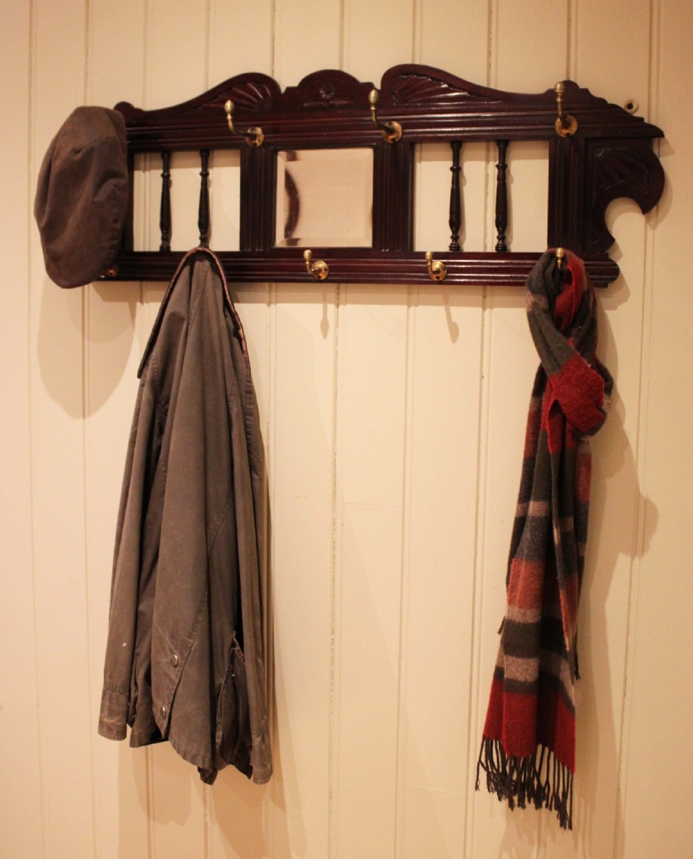 A late 19th-century dark mahogany wall-mounted coat rack featuring turned wooden spindles, a central square mirror, carved crest details, and ten brass hooks. View IV
