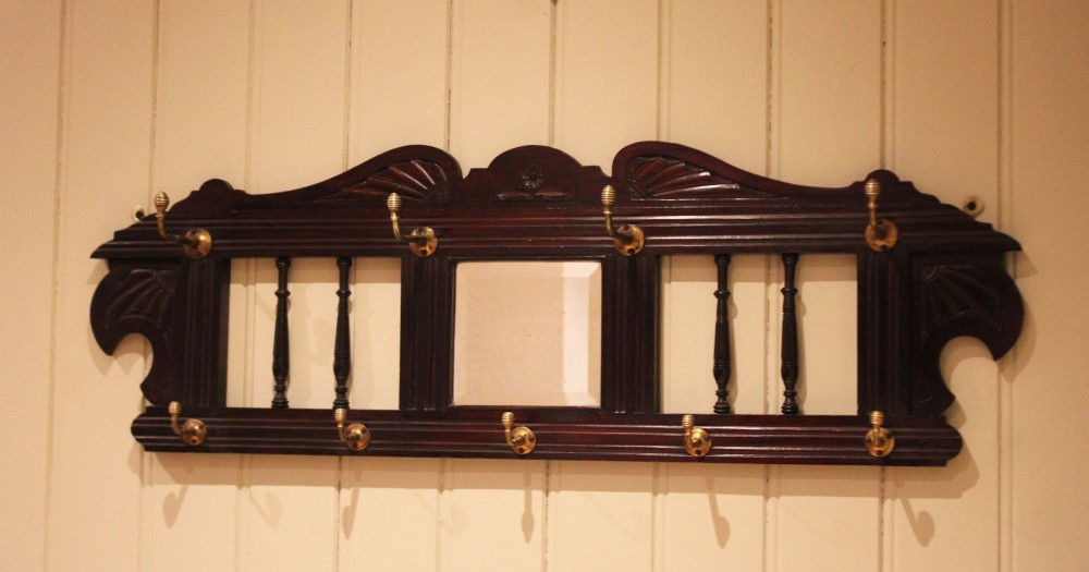 A late 19th-century dark mahogany wall-mounted coat rack featuring turned wooden spindles, a central square mirror, carved crest details, and ten brass hooks. View VII