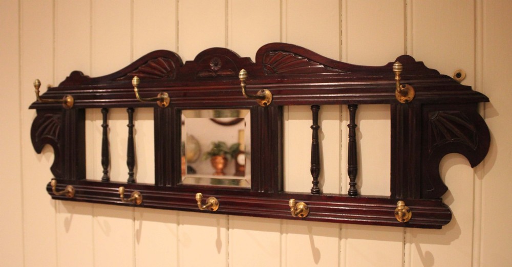 A late 19th-century dark mahogany wall-mounted coat rack featuring turned wooden spindles, a central square mirror, carved crest details, and ten brass hooks. View IX