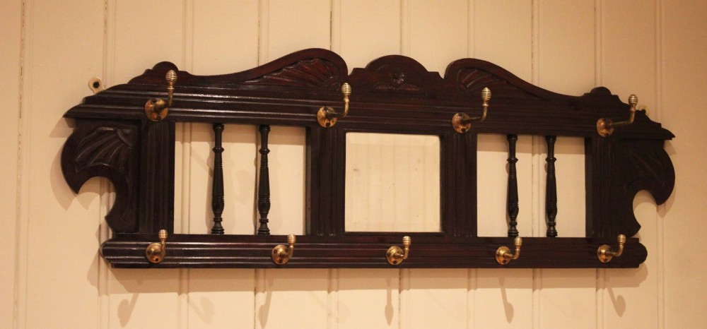 A late 19th-century dark mahogany wall-mounted coat rack featuring turned wooden spindles, a central square mirror, carved crest details, and ten brass hooks. View XI