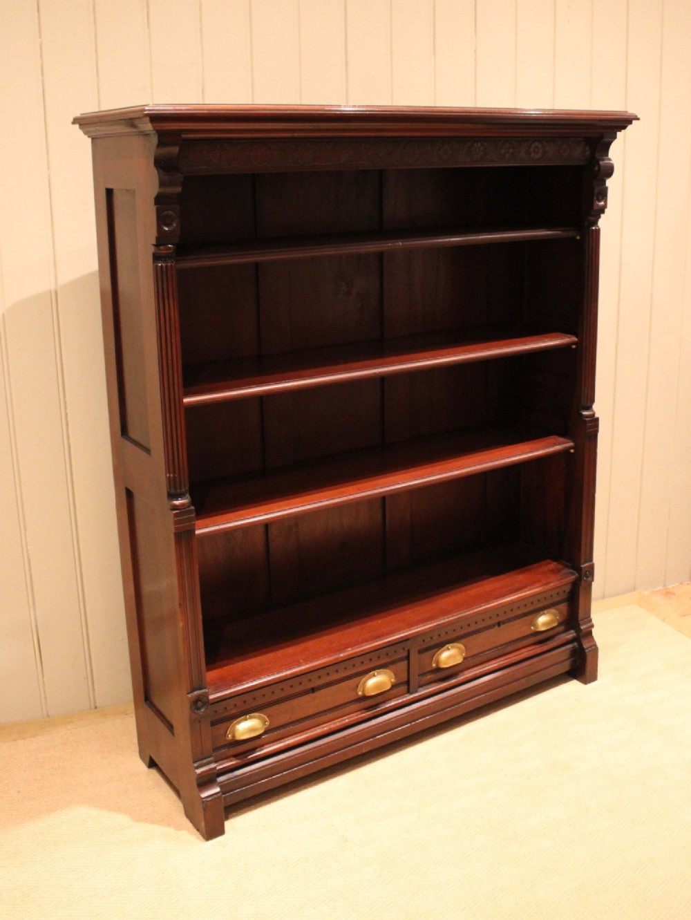 A large late Victorian dark mahogany open bookcase featuring four tiered shelves and two lower drawers with brass cup handles. View II