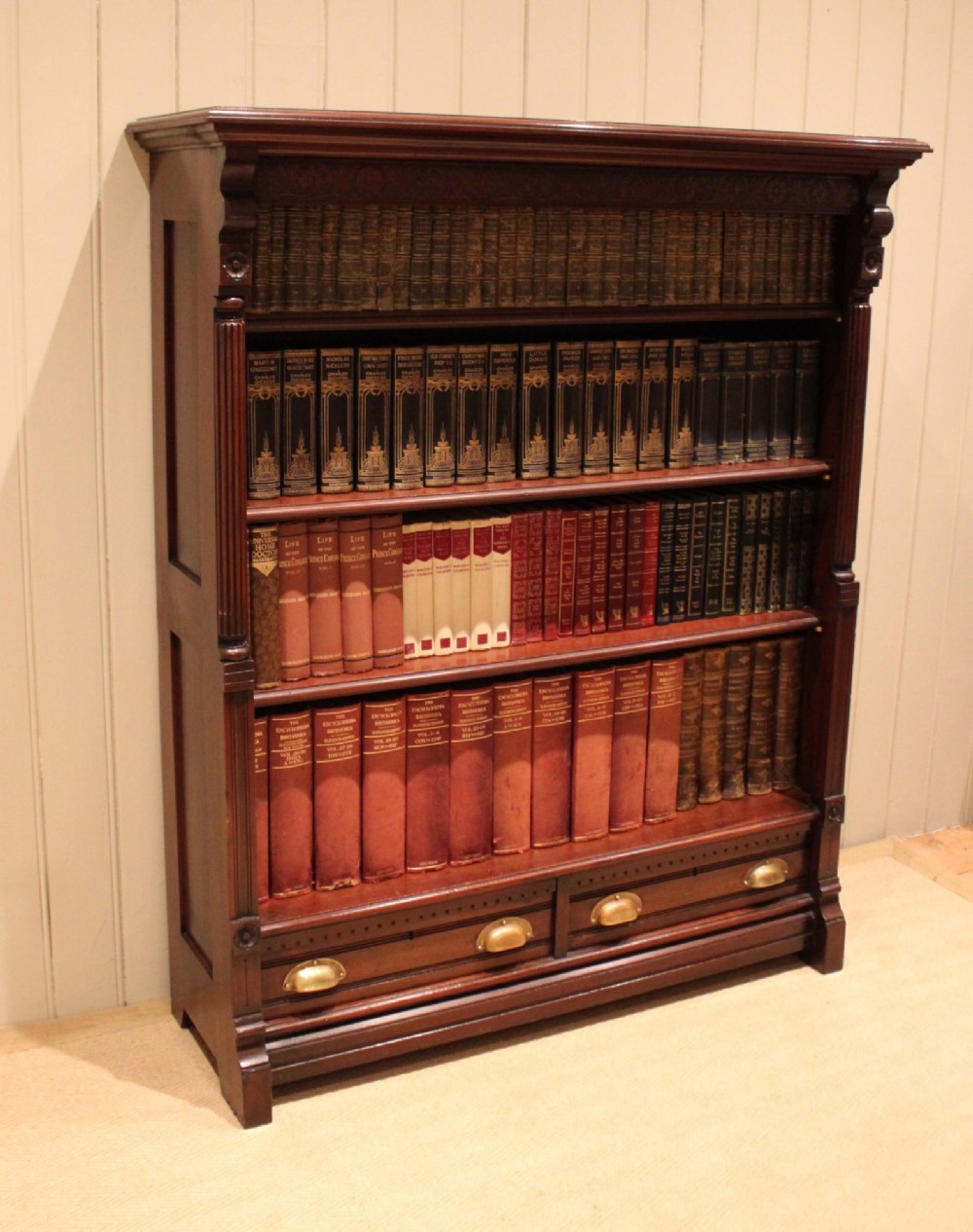 A large late Victorian dark mahogany open bookcase featuring four tiered shelves and two lower drawers with brass cup handles. View V