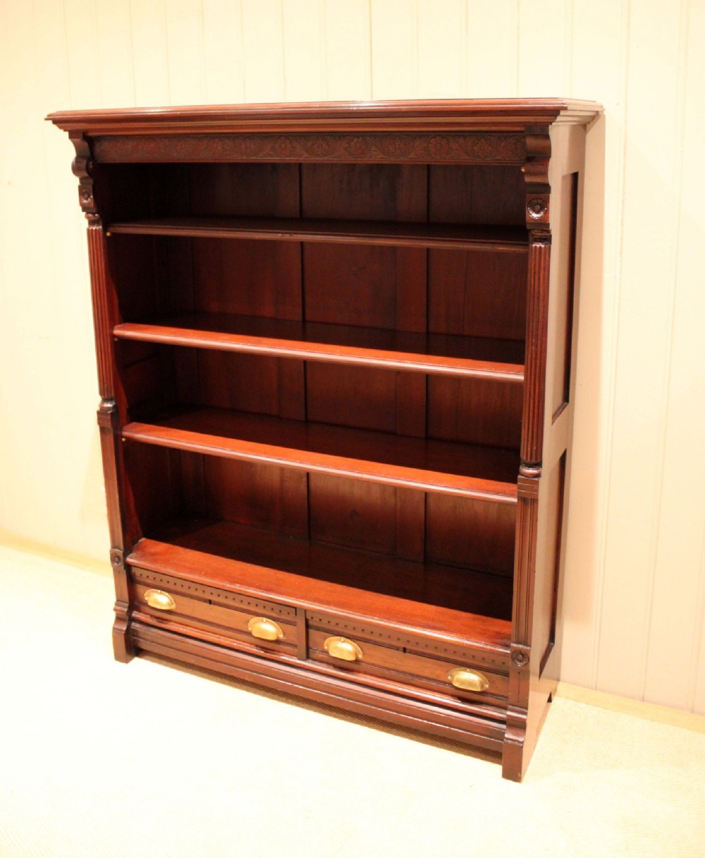 A large late Victorian dark mahogany open bookcase featuring four tiered shelves and two lower drawers with brass cup handles. View VI