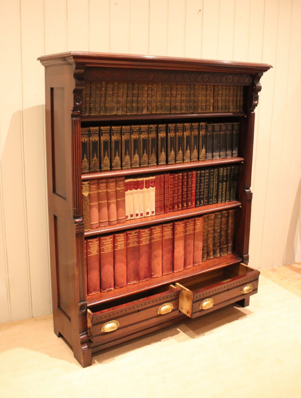 A large late Victorian dark mahogany open bookcase featuring four tiered shelves and two lower drawers with brass cup handles. View VII