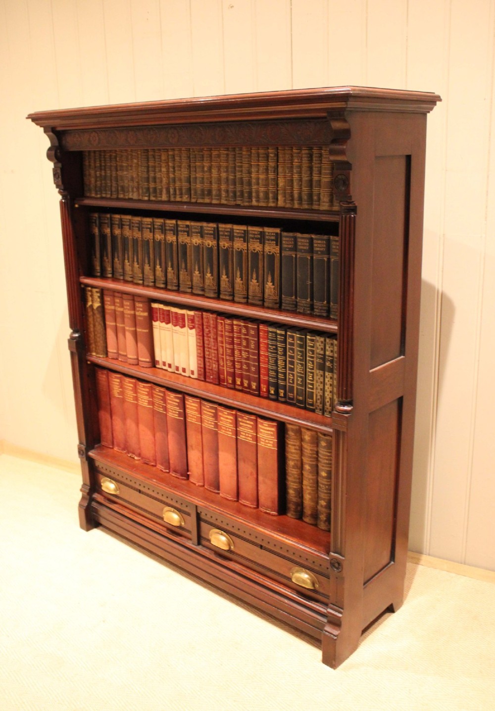 A large late Victorian dark mahogany open bookcase featuring four tiered shelves and two lower drawers with brass cup handles. View IX