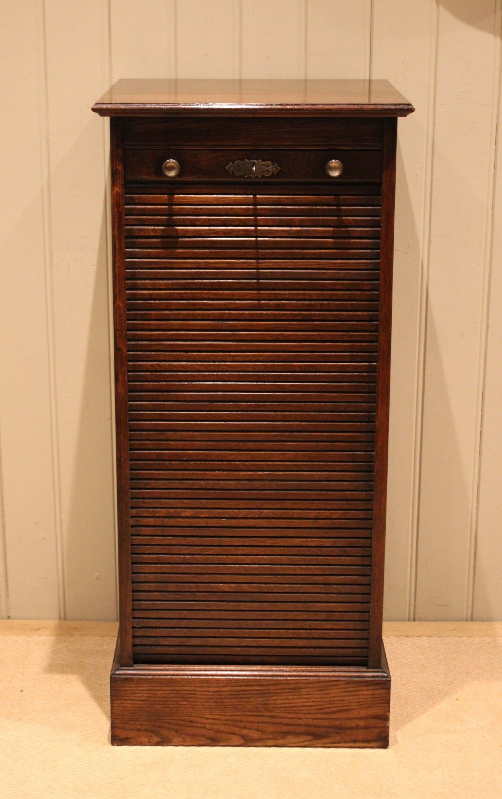 A tall dark oak single-column filing cabinet featuring a slatted wooden tambour front with top brass pull knobs and a keyhole escutcheon. View V