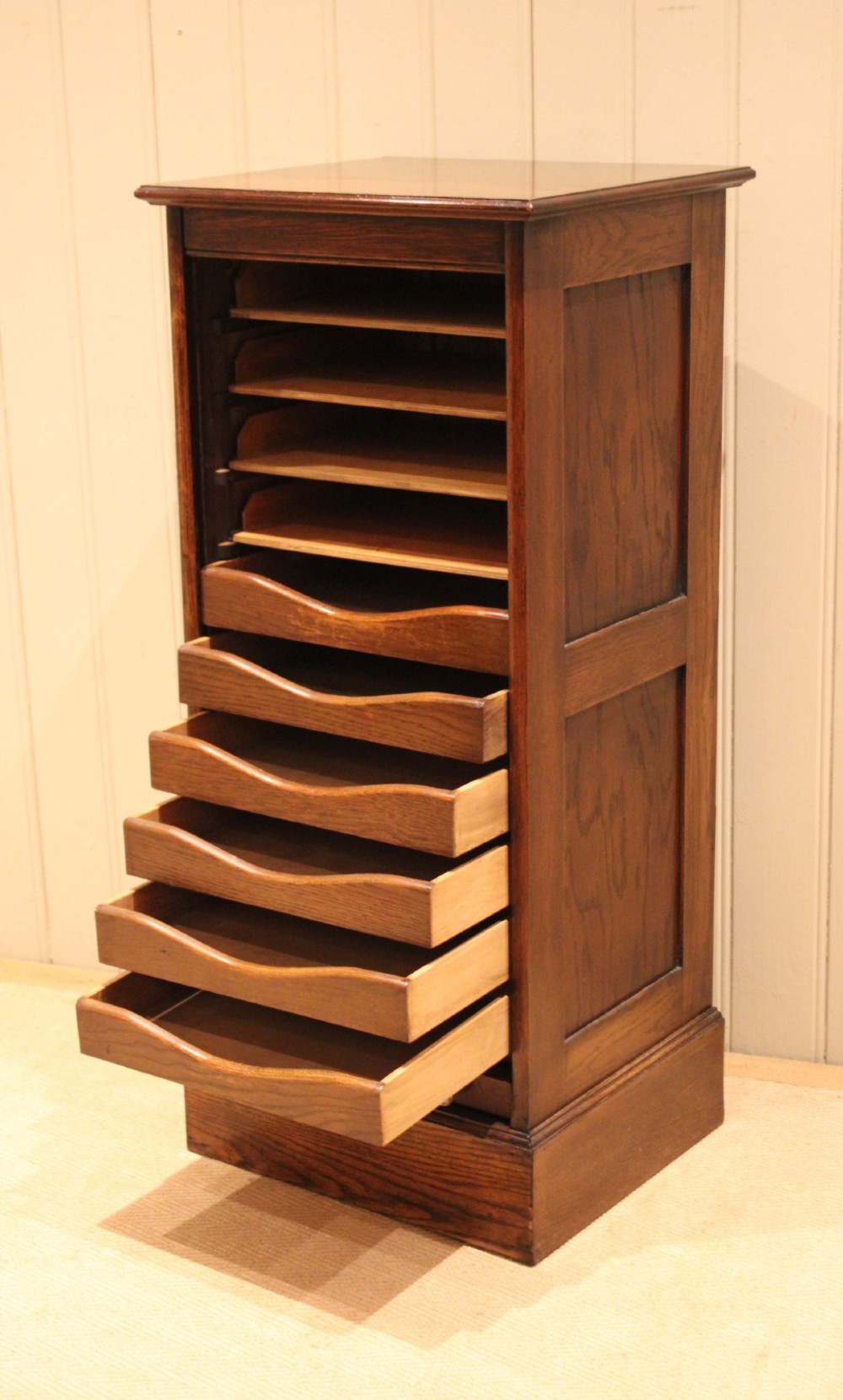A tall dark oak single-column filing cabinet featuring a slatted wooden tambour front with top brass pull knobs and a keyhole escutcheon. View VI