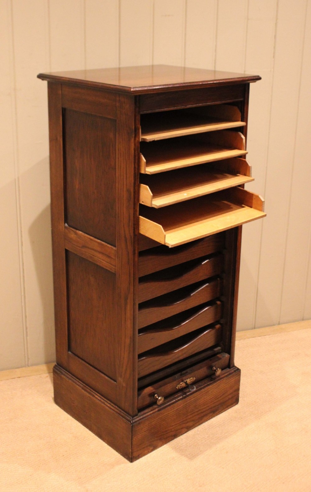 A tall dark oak single-column filing cabinet featuring a slatted wooden tambour front with top brass pull knobs and a keyhole escutcheon. View IX