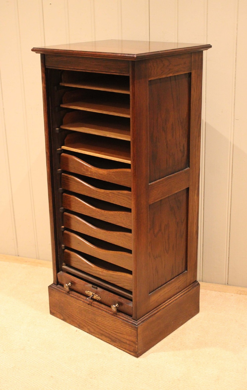 A tall dark oak single-column filing cabinet featuring a slatted wooden tambour front with top brass pull knobs and a keyhole escutcheon. View X
